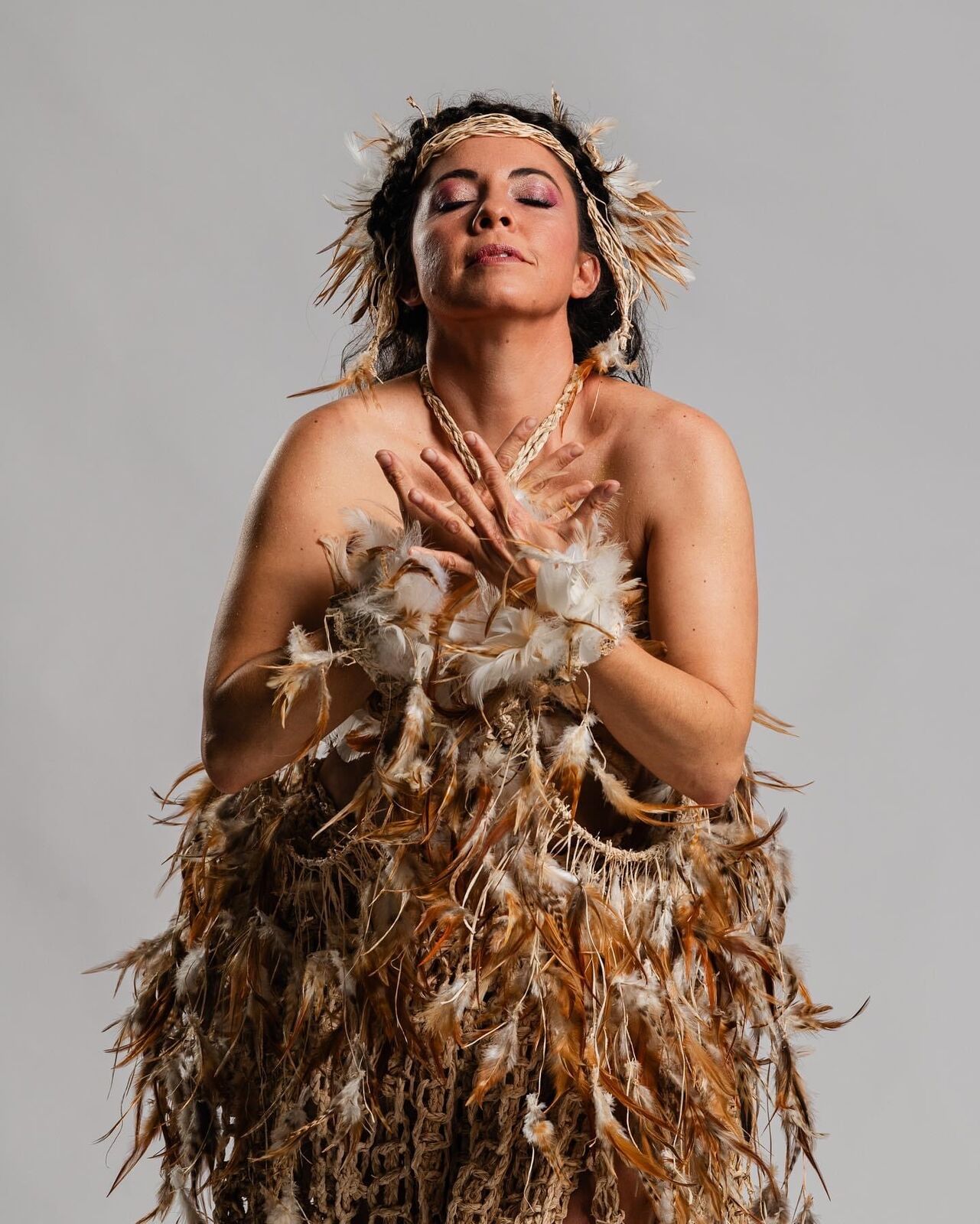 Alpha with her eyes closed in a feathered costume